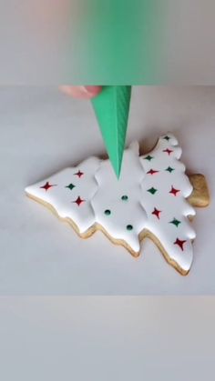 a cookie decorated with white and green icing is being cut into the shape of a christmas tree