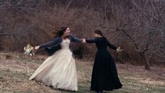 two women dressed in black and white are holding hands as they walk through the woods