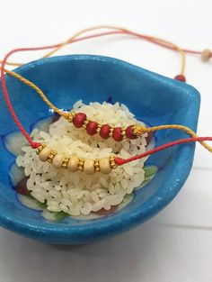 two necklaces sitting in a blue bowl with white rice and red beads on it