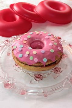 a pink frosted doughnut sitting on top of a glass plate next to red donuts