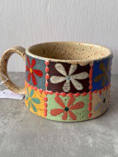 a ceramic cup with flowers painted on it and a tag attached to the handle, sitting on a table