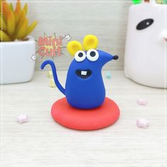 a blue toy with eyes and ears on top of a red object next to a potted plant