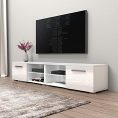 a white entertainment center with a large television mounted on it's side and a vase filled with flowers