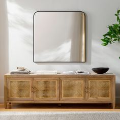 a wooden sideboard with a mirror on the wall and a potted plant next to it