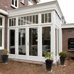 a large white house with many windows and plants in front of the house on a brick patio