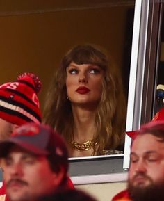 a woman wearing a red hat looking at her reflection in the mirror while others watch