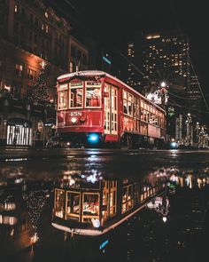 a red trolley car traveling down a street next to tall buildings in the city at night