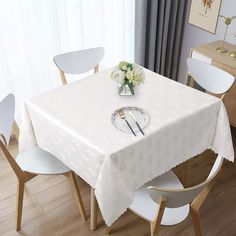 a white table cloth with silverware and flowers on it in front of a window