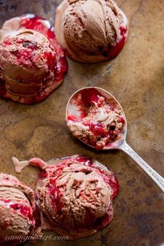 three scoops of chocolate ice cream with cranberry sauce on top and spoon next to them