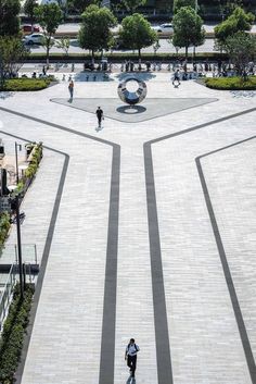 two people are walking around in the middle of a square with many trees and bushes