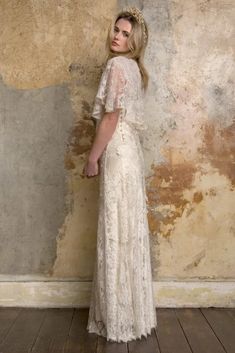 a woman standing in front of a wall wearing a white dress with short sleeves and a floral crown on her head