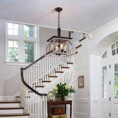 a white staircase in a house with wood floors and windows on the wall, next to a table with two vases filled with flowers