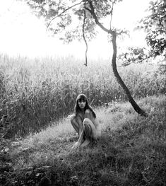 a woman sitting in the grass next to a tree