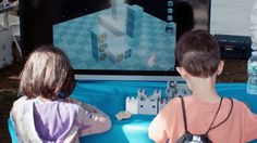 two young children sitting at a table playing with a game on the computer screen in front of them