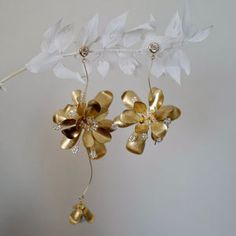 a gold and white flower is hanging from a branch with two bells attached to it