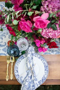 the table is set with blue and white plates, silverware, and pink flowers