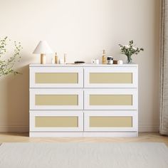 a white dresser sitting in front of a window next to a rug and lamp on top of a wooden floor