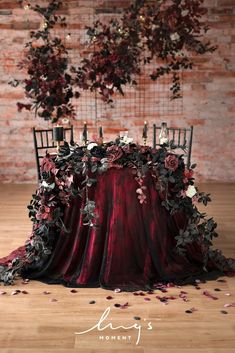 the table is covered with red and black cloths, surrounded by floral arrangements that are hanging from the brick wall