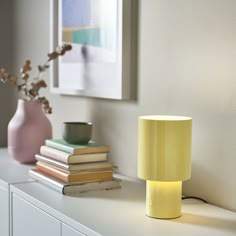 a yellow lamp sitting on top of a white shelf next to a vase and books