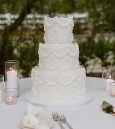 a white wedding cake sitting on top of a table next to silverware and candles