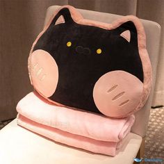 a black and pink cat pillow sitting on top of a white toilet next to two folded towels