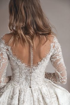 the back of a woman's wedding dress with beaded detailing and sheer sleeves