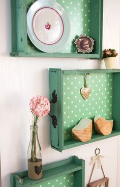 two green wooden shelves with plates and vases on them, one is holding flowers