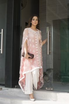 a woman standing on steps in front of a glass door wearing a pink top and white pants