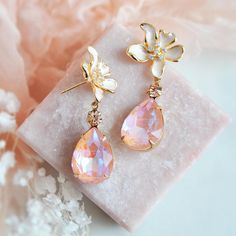 Add a dash of electric sparkle with these gorgeous flower earrings! The organic flowing flower earring posts are created with off white enamel and accented with tiny cubic zirconia. Secured to the flowers are shimmering faceted peachy pink teardrops set inside of vintage raw brass bezels which have a warm patina finish adding to their vintage charm. Embellished to the teardrops are tiny faceted champagne colored crystals for added sparkle. Whether adding these peach pink earrings for a lovely to Elegant Pink Teardrop Flower Earrings, Feminine Crystal Drop Earrings For Wedding, Pink Pearl Drop Earrings For Wedding, Pink Feminine Pearl Earrings For Wedding, Feminine Pink Pearl Earrings For Wedding, Pink Dangle Flower Earrings For Wedding, Pink Teardrop Pearl Earrings For Wedding, Pink Drop Flower Earrings For Formal Occasions, Pink Formal Flower Drop Earrings