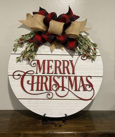 a merry christmas sign on top of a wooden table with red and green bows hanging from it