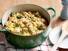 a green pot filled with pasta and broccoli on top of a wooden table