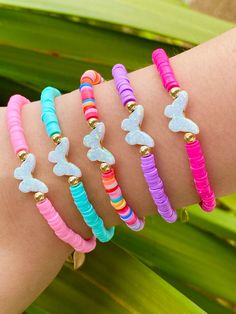 four different colored bracelets with butterfly charms on each arm and one has a gold bell