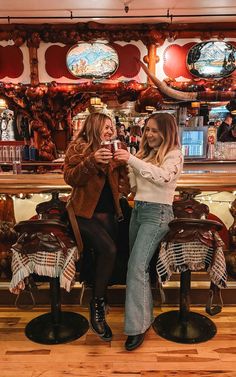 two women sitting on stools in front of a bar and one is holding a cell phone