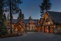 a large stone and wood house in the woods at night with lights on it's windows