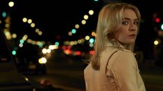 a woman standing on the side of a road at night with traffic lights in the background