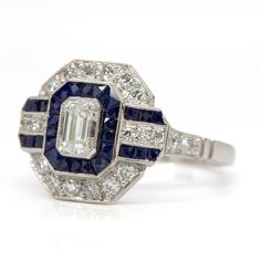 The Seraphina ring is a piece handmade in platinum which centers one emerald cut diamond of G color and VS1 clarity that weighs 0.50ctw. The center stone is surrounded by 24 old mine cut diamonds of G color and VS1 clarity that weigh 0.50ctw and 28 natural calibrated French cut sapphires that weigh 1.30ctw. Octagon Brilliant Cut Sapphire Ring With Diamond, Gia Certified Emerald Cut Art Deco Diamond Ring, White Gold Octagon Sapphire Ring With Brilliant Cut, White Gold Sapphire Ring With Brilliant Octagon Cut, Gia Certified Emerald-cut Platinum Cluster Ring, Gia Certified Emerald Cut Platinum Cluster Ring, Brilliant Cut Octagon Sapphire Ring In Platinum, White Gold Sapphire Ring With Square Cut Diamond, Square Cut Sapphire Ring In White Gold With Diamonds