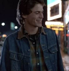 a young man standing in front of a building at night with his eyes closed and wearing a denim jacket