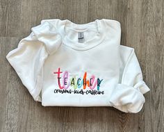 "Colorful Embroidered TEACHER Sweatshirt, Teacher Sweatshirt, Teacher Appreciation Gift for Teacher Valentine Gift, School Teacher Shirt HOW TO ORDER:  1) From the first dropdown menu, select sweatshirt size 2) From the second dropdown menu, select sweatshirt color 3) Click \"Add to Cart\" SIZING & SWEATSHIRT INFO: - Embroidery design is 5x7, the design will appear smaller on larger shirts - Larger Fit. If between sizes, we recommend sizing down - Sweatshirts are 18000 Gildan® Heavy Blend™ Adult Crewneck Sweatshirts IMPORTANT ORDERING INFORMATION: - Please review the sizing charts, with measurements, that are in the listing photos before purchasing.  CANCELLATIONS: - Cancellations are accepted within 24 hours of placing your order. After that, your order is possibly in production and we ca School Spirit Tops With Letter Embroidery, Long Sleeve T-shirt With Multicolor Embroidery, School Spirit Embroidered Cotton Sweatshirt, Cotton Sweatshirt With School Spirit Embroidery, Long Sleeve Sweatshirt With School Spirit Embroidery, White Letter Embroidery Sweatshirt For School, Embroidered Cotton Sweatshirt For School Spirit, Long Sleeve T-shirt With Letter Embroidery For School Spirit, White School Spirit Tops With Letter Embroidery