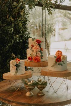 three tiered wedding cakes with flowers and greenery on the top are sitting on wooden tables