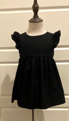 Beautiful handmade custom dress made from Black premium kona cotton fabric a bit fancier than the regular kona cotton has a slight sheen.  Cute little black flutter sleeve dress that buttons in the back. All seams are finished.  If you need the length of the dress to be different please include a message with order.   If you would like this made in a different color kona Cotton please message me, I would be happy to create a custom order for you. This is a beautiful dress for any special occasion. Wedding, funeral, graduation  or any occasion needing a cute black dress.  This dress can now be ordered with or without flutter sleeves. This dress can be monogrammed for an additional charge.  Measurements for the dress. size , length, 3 months  length 12.5". 6 months, length 14.5". Size, Chest Dress Flutter Sleeves, Cute Black Dress, Dress Baby Girl, Custom Dress, Kona Cotton, Flutter Sleeve Dress, Dress Girls, Custom Dresses, Flutter Sleeves