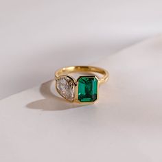 an emerald and diamond ring sitting on top of a white surface