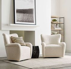 two white chairs sitting next to each other on top of a rug in front of a fireplace