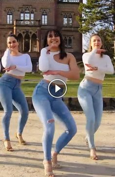 three women in jeans and white shirts are dancing on the street with their arms around each other