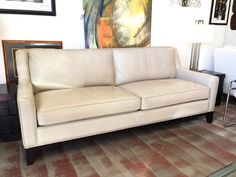 a white leather couch sitting on top of a carpeted floor next to a painting