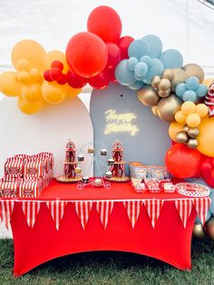 a red table topped with lots of balloons and desserts next to a white tent