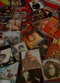 a pile of various cd's laying on top of each other in front of a red wall