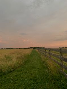 a wooden fence in the middle of a grassy field with tall grass on both sides