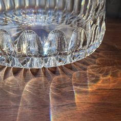 a clear glass bowl sitting on top of a wooden table next to a light shining through it