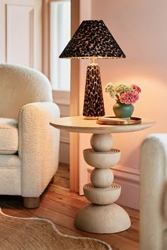 a table with a lamp on top of it next to a white chair and flower pot