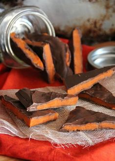 several pieces of chocolate peanut butter bars on a red cloth next to a glass jar